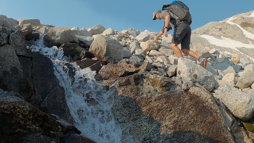 hiker climbing boulder field along flowing waterfall cascades in wallowa mountains oregon