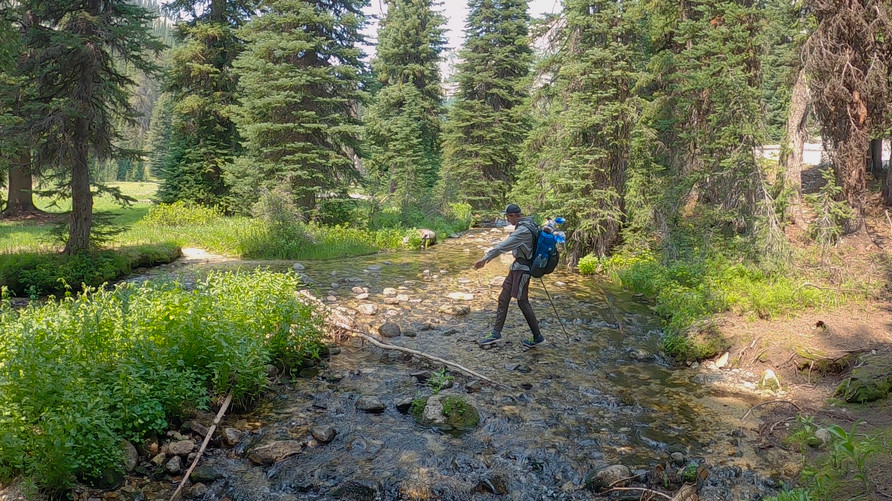 hiker fording minam river in the wallowa mountains on a backpacking trip
